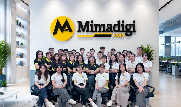 Nhân sự MIMA ngồi thành nhiều hàng trước bảng hiệu Mimadigi trong văn phòng