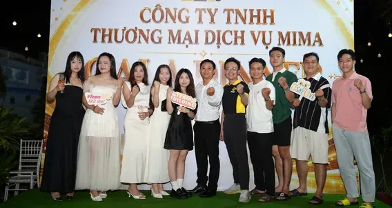 Một nhóm nhân sự cầm bảng chữ chụp ảnh trước phông tiệc cuối năm của công ty