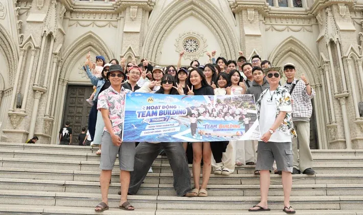 Cả công ty cầm băng rôn team building chụp ảnh trên bậc thềm nhà thờ Núi